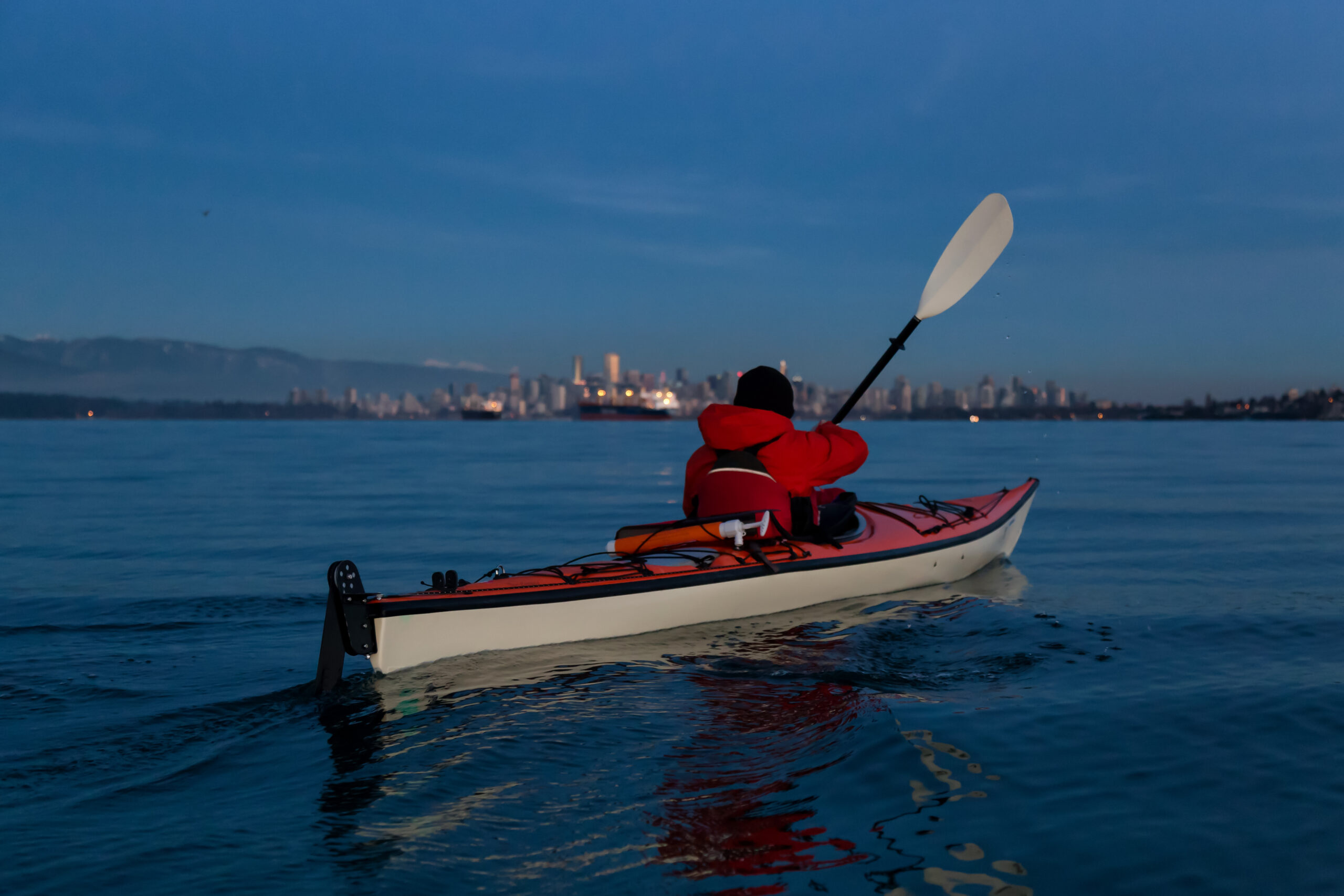 Adventure Man on a Sea Kayak is paddline during a vibrant winter sunset with Downtown City Skyline in the background. Taken in Vancouver, British Columbia, Canada.