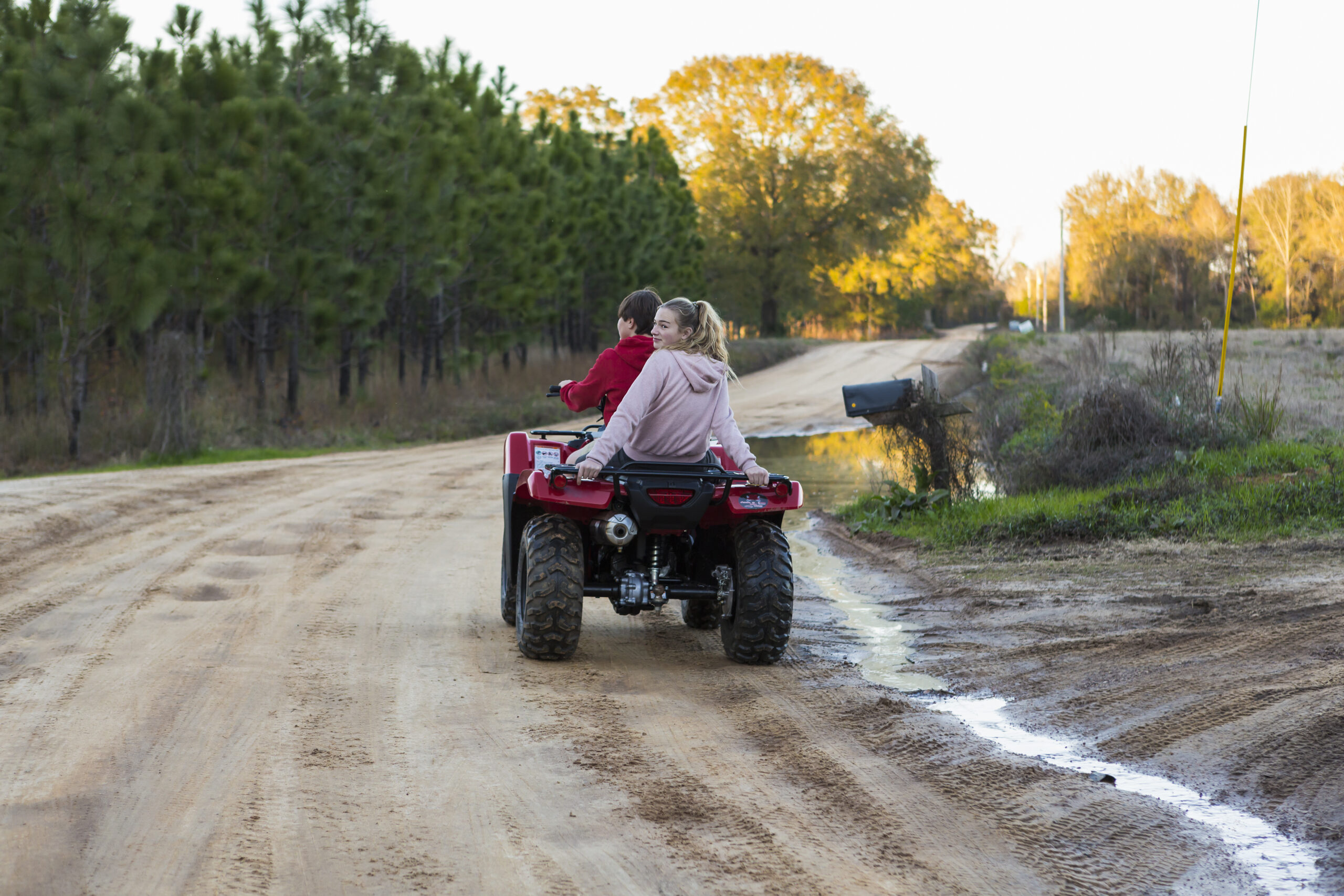Two teenagers riding on a buggy, all terrain vehicle on a muddy track.