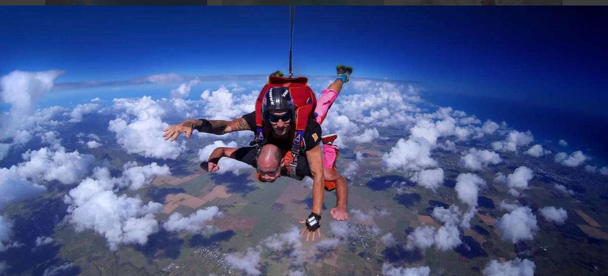 Skydiver gliding above fluffy clouds with a backdrop of ocean and sky