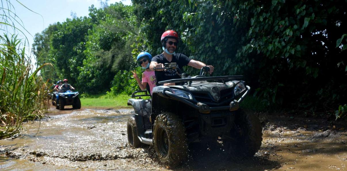 Couple riding a quad bike through a muddy trail in Mauritius