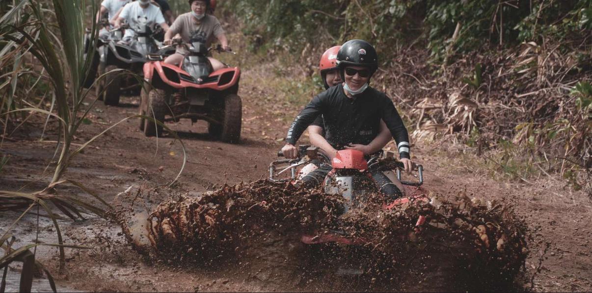 Group of tourists riding quad bikes through muddy forest terrain