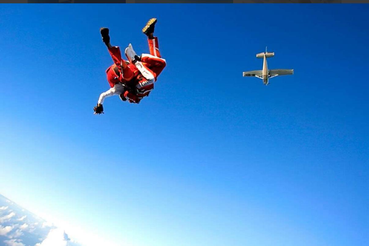 A skydiver in free fall as the aircraft flies above in a clear blue sky