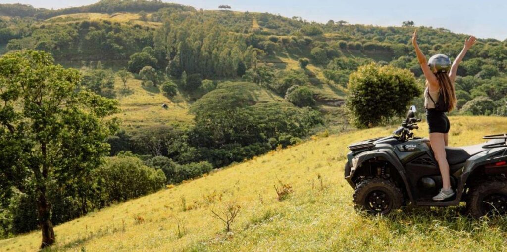 Tourist raising hands on quad bike with hilly landscape in Mauritius