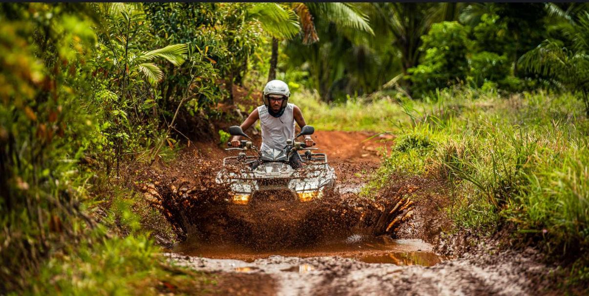 Rider driving quad through a muddy water trail in Mauritius forest