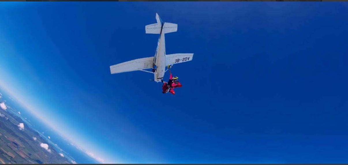 A plane flying above the Indian Ocean while a skydiver descends in Mauritius